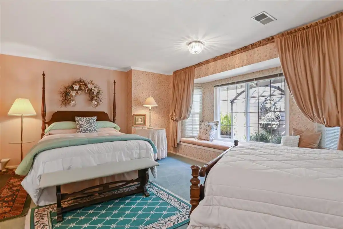 A queen bed sits beside a large window against a backdrop of peach-colored floral wallpaper.