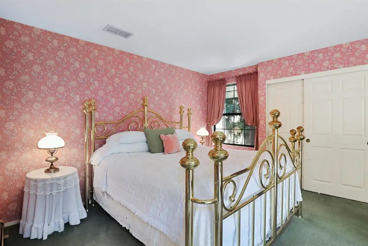 King sized bed on a brass frame against a rose colored floral wallpaper.