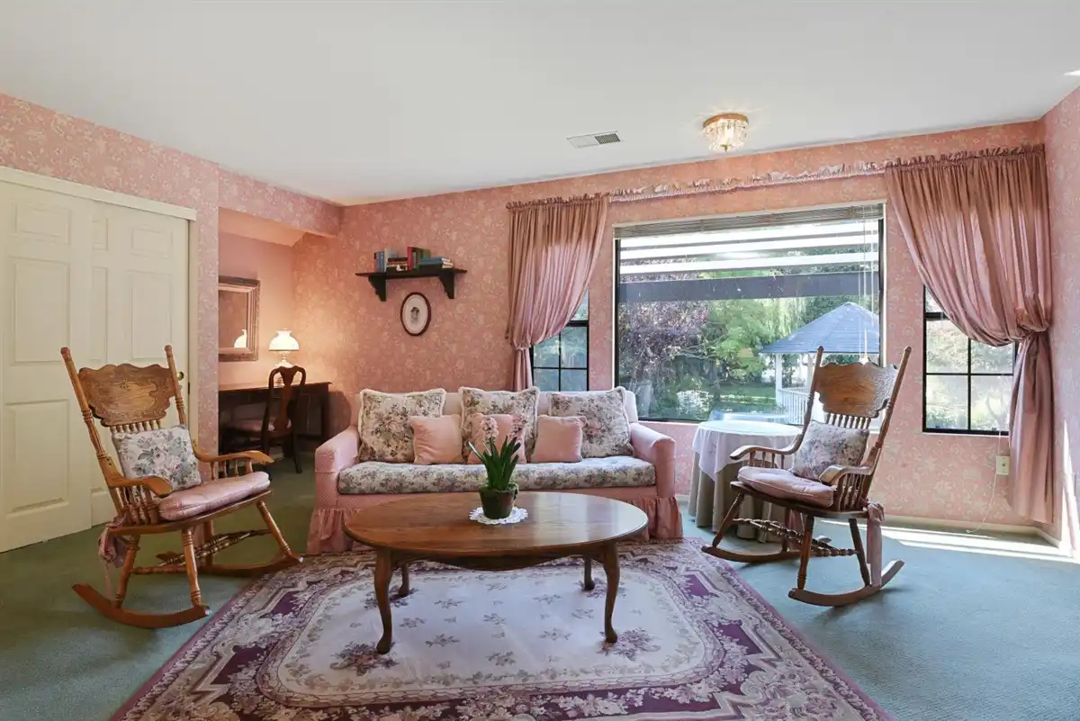 Floral patterned couch between two rocking chairs, positioned next to a wooden table.