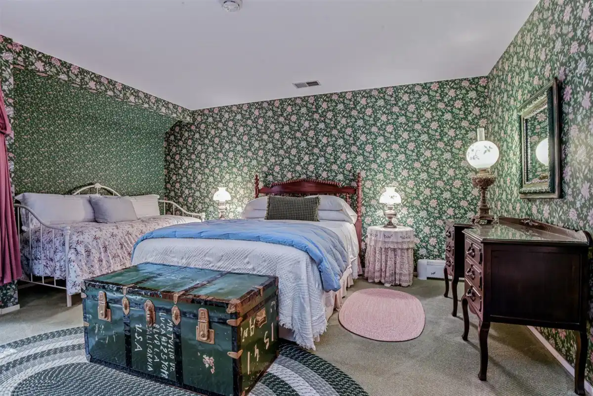 A queen bed nestled between two bedside tables against green floral wallpaper.