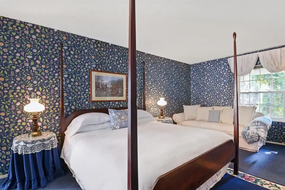 A king sized bed in a wooden frame against a blue floral wallpaper.